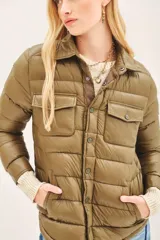 Campera puffer color beige con cuello camisero, cierre con botones a presión, bolsillos con solapa en el pecho y relleno de plumas.
