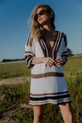 Vestido corto tejido en hilo de algodón color blanco con rayas horizontales marrones y negras, escote en V y mangas cortas.