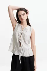 Blusa sin mangas color beige con lazo frontal y textura liviana.