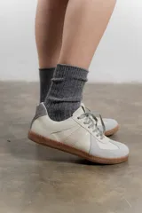 Zapatillas urbanas de cuero color crema con puntera y talón en gamuza gris, suela de goma marrón y cordones grises.