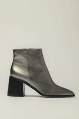 Botín de cuero metalizado color peltre con punta fina y cierre lateral. Tiene taco geométrico de madera color negro.