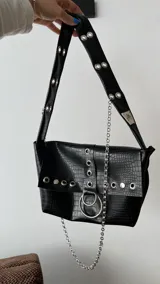 Cartera negra con textura símil cocodrilo, con herrajes plateados y cadena decorativa.