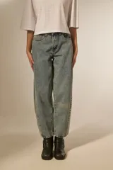 Pantalón de jean azul claro, estilo barrel y de calce bajo, con detalles de tachas metálicas en los laterales y en la cintura.