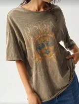 Remera marrón con cuello redondo y mangas cortas, con estampado de un sol con rostro en tonos ocre y azul. Corte holgado y estilo vintage.