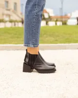 Botín Chelsea de cuero negro, con elástico lateral acanalado y detalle de cuero charol en el talón. Posee punta cuadrada y taco ancho y bajo.