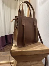 Cartera tote de cuero vacuno color marrón con laterales de cuero con pelo de vaca blanco y marrón. Tiene doble asa corta y correa larga desmontable.