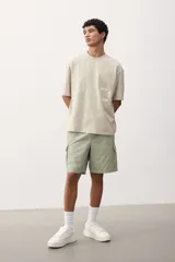 Short cargo color verde claro en popelina de algodón, con cintura elástica ajustable con cordón, bolsillos laterales, bolsillos cargo con solapa y botón a presión en piernas y traseros, y aberturas laterales en el bajo.