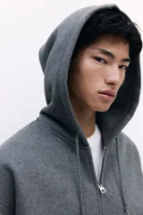 Campera con capucha de tejido pesado de mezcla de algodón, color gris oscuro jaspeado, con interior cepillado suave. Modelo con hombros caídos, capucha forrada en punto con cordón para ajustar, cierre frontal y bolsillos canguro. Puños y bajo acanalados. Corte oversized.