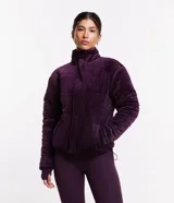Campera deportiva de terciopelo color violeta, con cuello alto, cierre de botones, bolsillos laterales y puños ajustados.