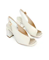 Sandalias de cuero color blanco hueso, con punta cuadrada y escote en el empeine. Tienen un tacón cuadrado de 7 cm y tira trasera con hebilla. El interior es de cuero color beige.