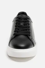 Zapatillas urbanas de cuero sintético negro con cordones y suela blanca de goma con volumen.