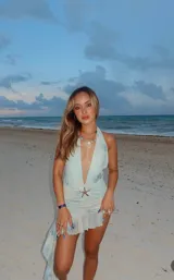 Minivestido celeste con estampado difuminado, escote halter con abertura en V y falda con volados. Presenta un aplique de estrella de mar en el centro.