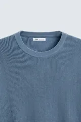 Jersey color crema de punto perlado, con cuello redondo, manga larga y corte regular fit.
