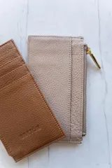 Tarjetero de cuero color rosa pálido con cierre de cremallera dorada y múltiples ranuras para tarjetas.