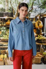 Blusa celeste de denim con cuello polo, manga larga y botones marrones.
