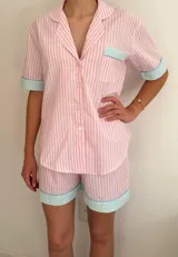 Conjunto de pijama de algodón a rayas verticales rosas y blancas, con detalles en celeste. Incluye camisa de manga corta con botones y bolsillo en el pecho, y shorts con cintura elástica.