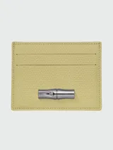 Tarjetero de cuero texturizado color amarillo pálido, con tres ranuras frontales para tarjetas y un cierre metálico tipo bambú en tono plateado.