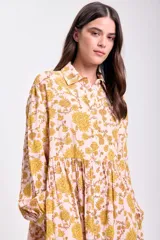 Vestido midi de corte holgado con estampado floral en tonos rosa y amarillo. Tiene cuello camisero, mangas largas con puños elásticos y falda escalonada.
