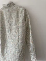 Camisa blanca estampada con flores pequeñas en tonos celeste, rosa y amarillo. Confeccionada en lino 100%, con botones de nácar y puntilla de algodón en los puños.