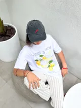 Remera blanca de algodón orgánico, corte oversize, cuello redondo y mangas cortas. Estampado frontal con diseño de limones, bebidas y texto en azul.