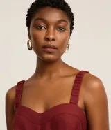 Mono de mujer color rojo oscuro (bordó), de corte recto y pierna ancha, con escote corazón y tirantes anchos con elástico. Presenta pliegues frontales que caen rectos hasta el ruedo.