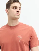 Remera verde con estampado en la espalda de una playa con palmeras y la frase "Ride the waves".