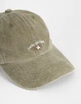 Gorra color beige con bordado frontal de la frase "Lucky Girl Club" y un trébol de cuatro hojas.