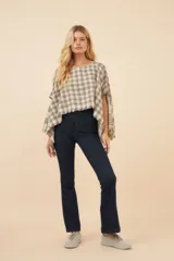 Poncho color beige con diseño a cuadros, cuello bote y terminaciones desflecadas. Tiene aberturas para los brazos en los laterales y detalles en cuero.