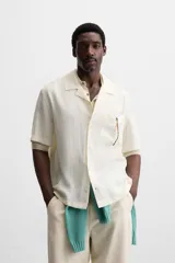 Camisa negra de corte relaxed fit, confeccionada en tejido con mezcla de modal. Tiene cuello bowling, manga corta, bolsillo de parche en el pecho y cierre frontal con botones.