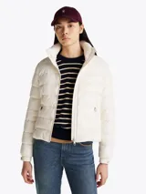 Campera Tommy Hilfiger color blanco, acolchada con plumón, de corte regular. Tiene cuello chimenea, capucha plegable, cierre de cremallera, dos bolsillos laterales con cremallera, puños elásticos con botones a presión y parche con el logo de la marca en la manga.