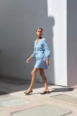 Vestido corto celeste con bordados calados, escote en V, mangas 3/4 abullonadas con elástico y cinturón con hebilla redonda de madera. Cierre frontal con botones.
