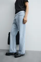 Pantalón de jean celeste de corte flare, con tiro medio, cinco bolsillos, cierre frontal con cremallera y botón, y bajo con acabado irregular.