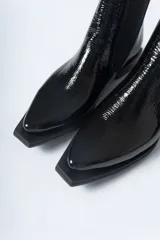 Botín Chelsea de mujer, color negro charol, con elástico lateral y punta cuadrada. Posee un taco bajo y plano.