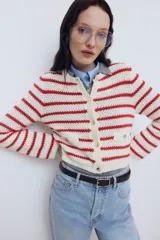 Cárdigan corto de punto texturizado a rayas rojas y blancas, con cuello redondo, cierre frontal con botones dorados y bolsillos decorativos con botón. Remate acanalado en cuello, tapeta, puños y bajo.