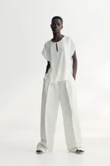 Blusa color blanco hueso de tejido de crepé de viscosa con cuello redondo y abertura de cerradura con botón de metal pequeño adelante. Mangas japonesas de corte raglán y bajo levemente redondeado.