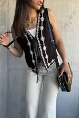Chaleco negro con bordado de flores blancas, escote en V y lazos de ajuste en el frente.