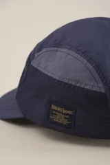 Gorro tipo cap verde con paneles de diferentes texturas y etiqueta con logo en el lateral.