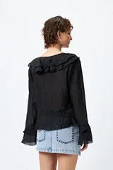 Blusa blanca de gasa con escote en V y volados en el cuello y las mangas largas. Se ata con lazos finos al frente.