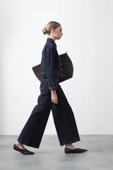 Pantalón de denim azul oscuro con corte flare, ajustado en la cadera y amplio en el ruedo. Presenta pespuntes a contratono en color blanco que resaltan las costuras.