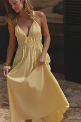 Vestido midi amarillo de tejido fluido con escote pico y tirantes finos cruzados en la espalda ajustables con lazada. Tiene detalle de elásticos bajo el pecho.