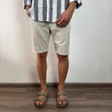 Bermuda color beige claro, estilo chino, confeccionada en gabardina. Presenta un corte recto y dobladillo en el ruedo.