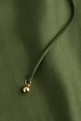 Vestido corto color verde oliva, de corte holgado, con cuello redondo fruncido, mangas globo largas con puños elásticos y botonadura frontal. Incluye cinturón fino para atar.