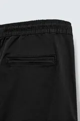 Pantalón cargo negro de corte slim fit, confeccionado en tejido de algodón con cintura elástica ajustable con cordón. Cuenta con bolsillos frontales, traseros y bolsillos tipo parche con solapa en los laterales.