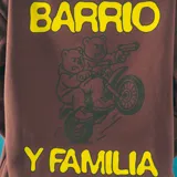 Canguro marrón con capucha y cordones ajustables, bolsillo tipo canguro y puños y cintura acanalados. Estampado amarillo en el pecho con la leyenda "Barrio y Familia".