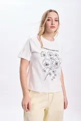 Remera blanca de algodón con cuello redondo y mangas cortas. Estampa de flores y texto en color negro.