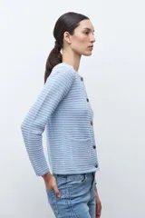 Chaqueta de punto color celeste claro, de manga larga y corte ajustado, con cuello redondo y cierre frontal de botones metálicos plateados. El tejido presenta un patrón texturizado horizontal.
