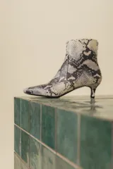 Botín blanco con estampado de piel de serpiente, punta fina y taco chupete. Cierre con cremallera en la parte trasera.