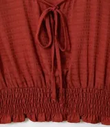 Blusa color ladrillo con escote redondo con ajuste, mangas largas con aberturas en los hombros y elástico en la cintura.