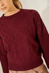 Sweater color borgoña de punto con cuello redondo, diseño de rombos con tachas aplicadas y detalle de corazones de cuero en la espalda.