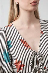 Blusa de silueta relajada con estampado de lunares negros sobre fondo crema. Cuenta con escote en V con lazos regulables, frunce bajo el busto y mangas cortas con volumen.
